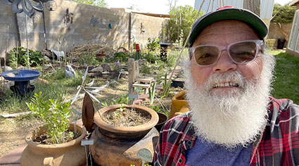 a bearded Rick Robb smiles for the camera in sunglasses with his garden behind him