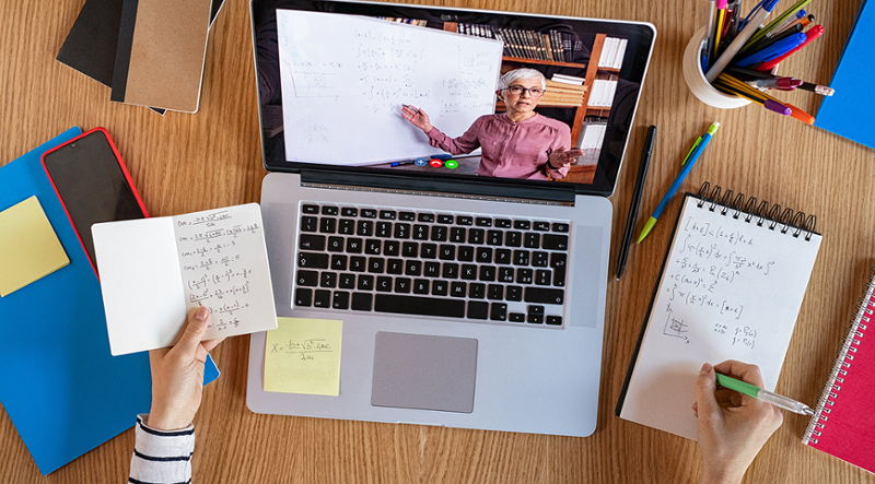 Someone looking a person talking on a laptop screen and making notes